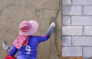 Rear view of female Construction worker plastering cement on concrete block wall