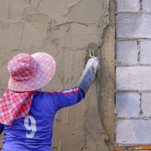 Rear view of female Construction worker plastering cement on concrete block wall