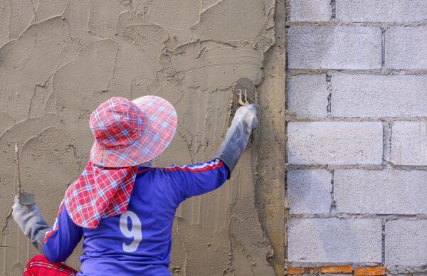 Rear view of female Construction worker plastering cement on concrete block wall