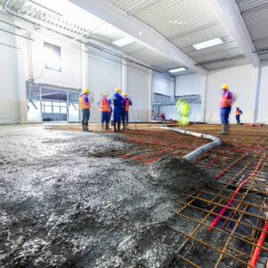 Workers do concrete screed on floor with heating in a new warehouse building